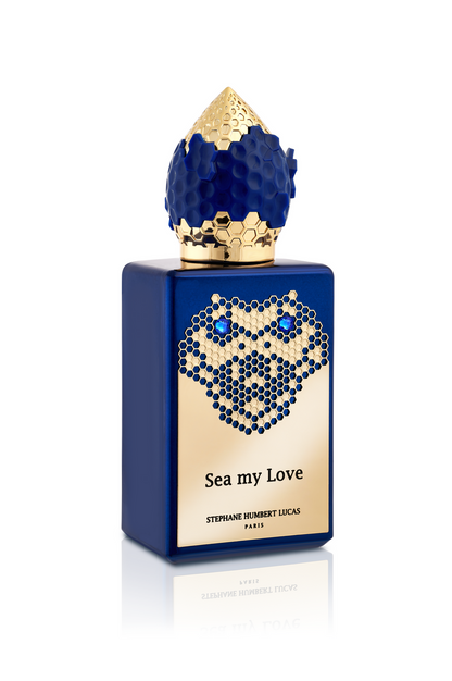 A blue perfume bottle with a gold honeycomb cap and gold label reading Sea My Love Eau de Parfum by Fragrapedia Haus, its jeweled design inspired by ocean legends.