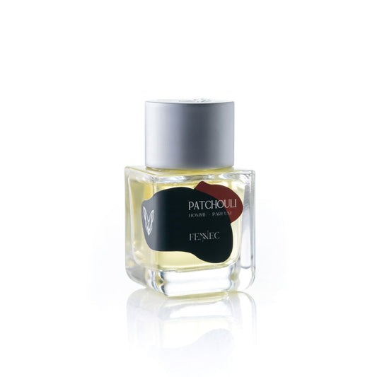 A clear glass perfume bottle with a silver cap contains yellow liquid. The label reads Patchouli EDP Fennec with a small fennec fox logo, evoking the spirit of patchouli and the North African desert.