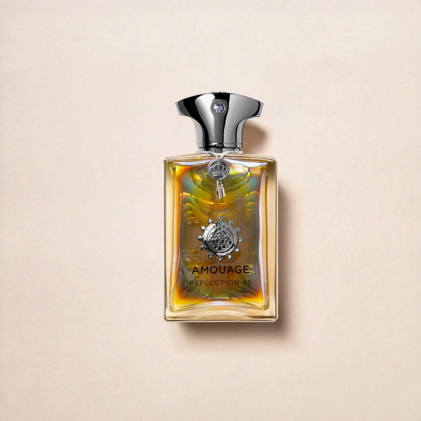 Reflection 45 Man Extrait de Parfum by Fragrapedia Haus is an exceptional woody floral musk scent, presented in a bottle with a shiny silver cap, decorative emblem, and iridescent golden-yellow liquid on a light beige background.