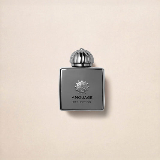 A sleek, metallic silver bottle of Reflection Woman Eau de Parfum by Fragrapedia Haus stands centered on a light beige background, its ornate cap evoking the white florals, musk, and woods found inside.