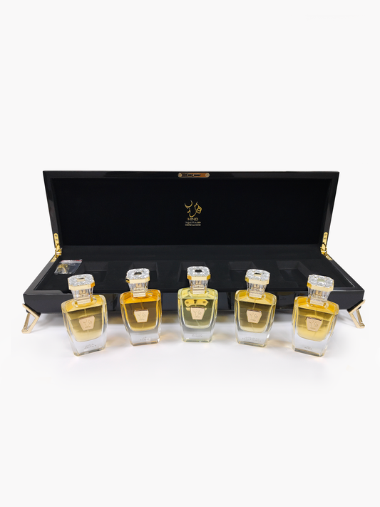 Five elegant perfume bottles from the Royal Precious Collection by Hind Al Oud, each with gold labels and crystal caps, are arranged before an open black luxury display box—an exquisite gift set showcased on a white background.