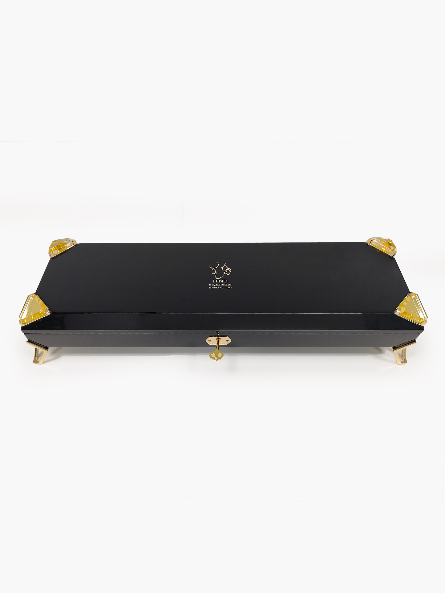 A sleek black rectangular box with gold accents, gold clasp, and gold feet features the Hind Al Oud logo and text on the lid, revealing it as the exclusive Royal Precious Collection perfume gift set by Hind Al Oud against a plain white background.