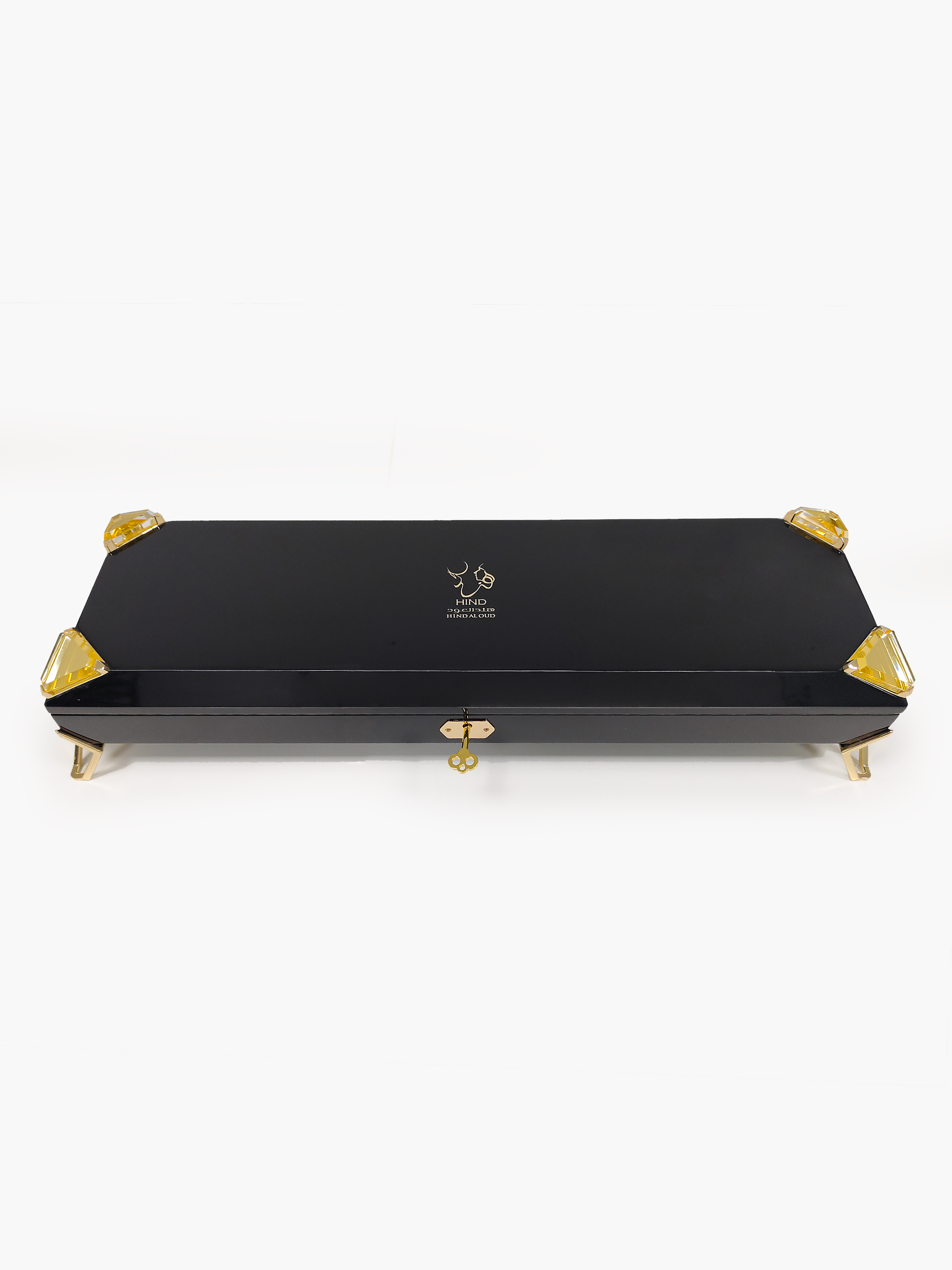 A sleek black rectangular box with gold accents, gold clasp, and gold feet features the Hind Al Oud logo and text on the lid, revealing it as the exclusive Royal Precious Collection perfume gift set by Hind Al Oud against a plain white background.