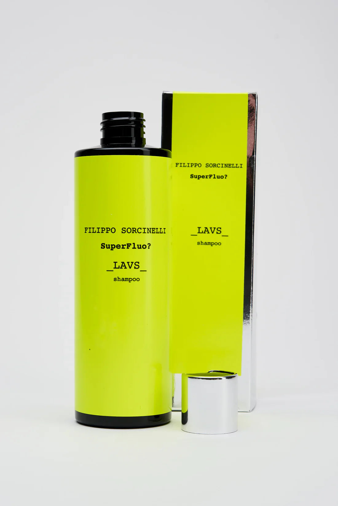 A bright yellow SUPERFLUO LAVS SHAMPOO bottle by Filippo Sorcinelli with a black cap and its matching box, both labeled with the product name, stand against a white background. The box features a sleek silver base.