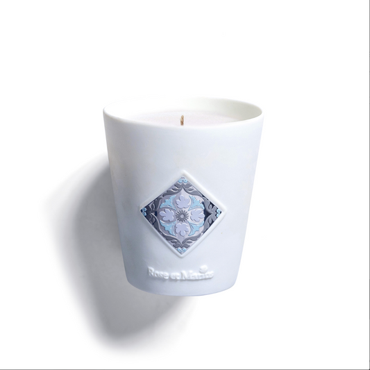 The AMBLING BENEATH THE ORATORY "SCENTED CANDLE UNE FLÂNERIE SOUS L'ORATOIRE" by Rose Et Marius comes in a white Limoges porcelain holder with blue and gray diamond tile design on the front, set against a plain white background.
