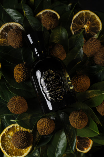 Dark bottle with intricate design on a bed of leaves and sliced oranges epico thelycheeus
