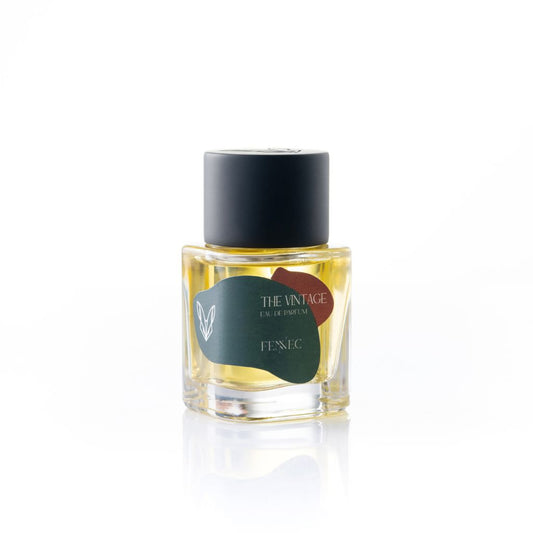 A small glass bottle of The Vintage EDP by Fennec, inspired by North Africa, with a black cap and golden liquid, is shown against a white background.