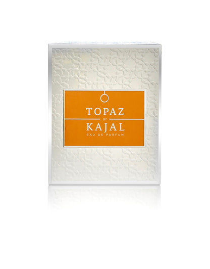 A white textured rectangular perfume box with an orange center label reads "Topaz Eau de Parfum - Kajal Perfumes Paris"—an elegant fragrance inspired by the allure of ruby jewelry and symbolizing love.