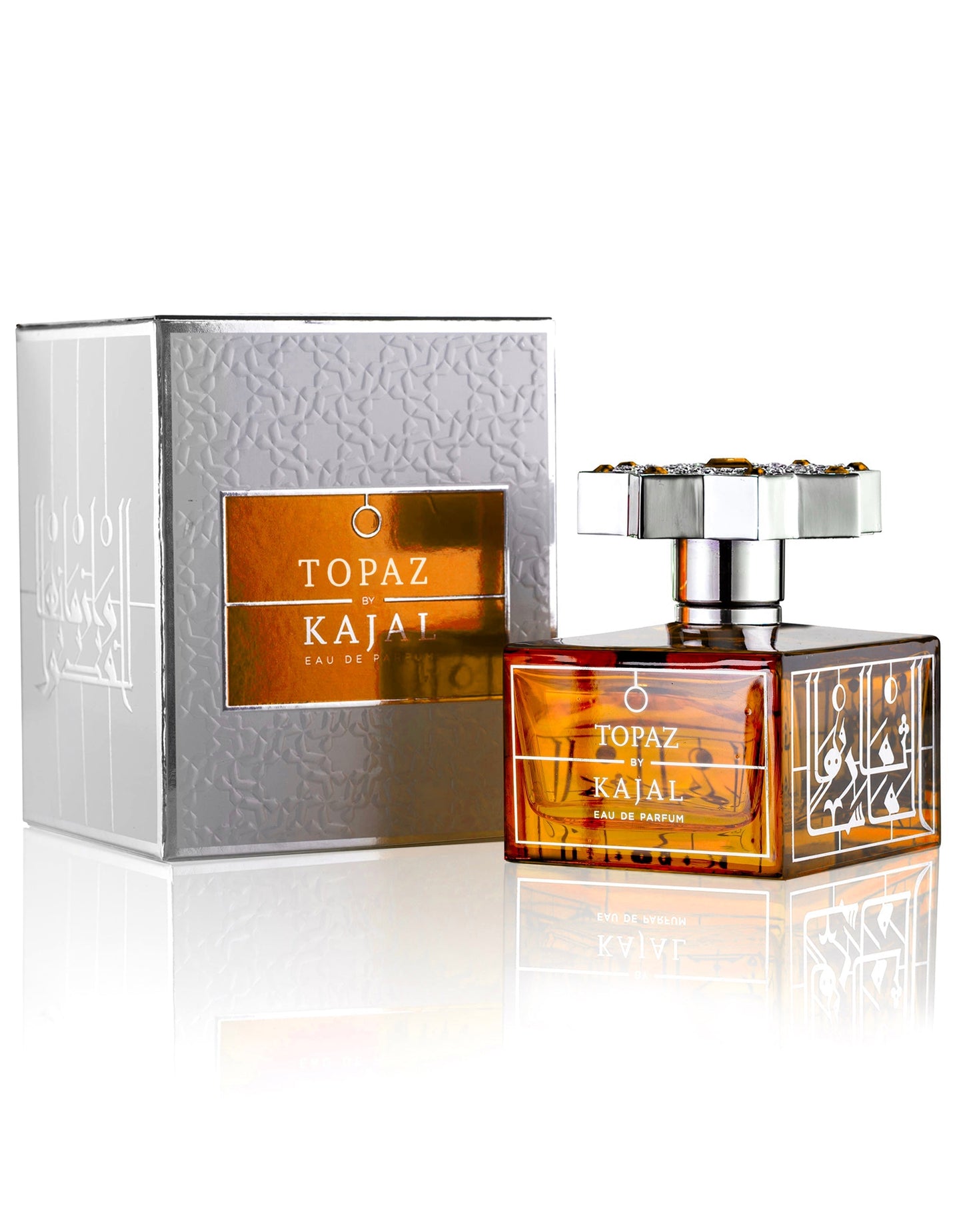 A bottle of Topaz Eau de Parfum by Kajal Perfumes Paris, with a silver flower-shaped cap, is displayed next to its matching silver and orange box—both adorned with elegant gold and white designs symbolizing eternal love.