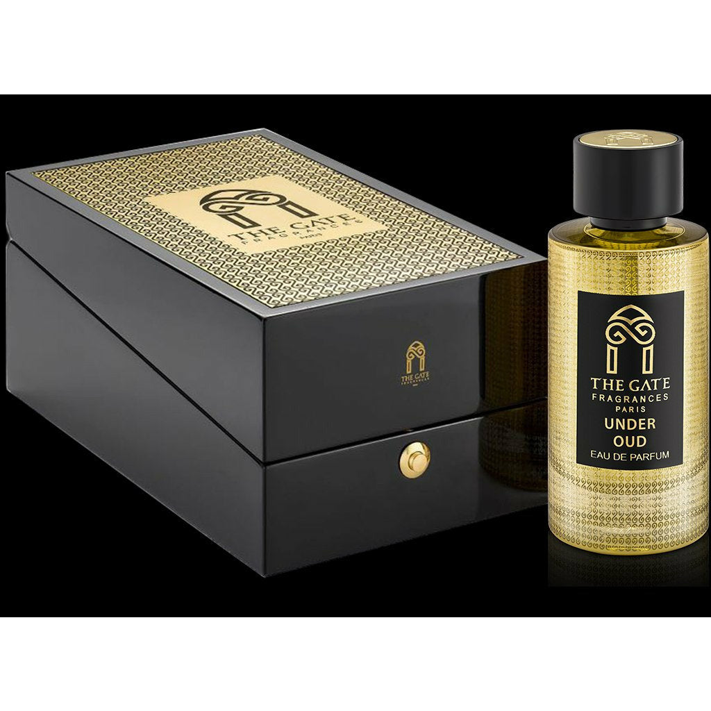 A gold and black bottle of Under Oud Eau de Parfum by The Gate Paris stands beside a matching box with a hinged lid and gold knob, both featuring The Gate Paris logo.