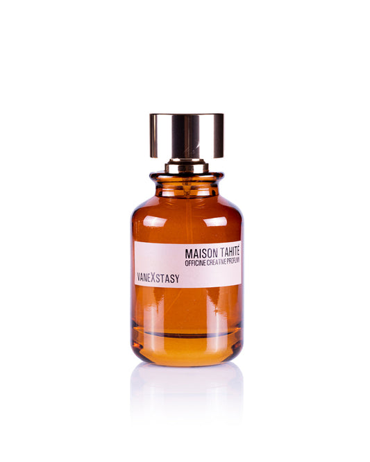 A brown glass bottle labeled Maison Tahite Vanexstasy Eau de Parfum stands upright on a white background, featuring a shiny gold cap and a scent blending creamy sandalwood with rich vanilla absolute.