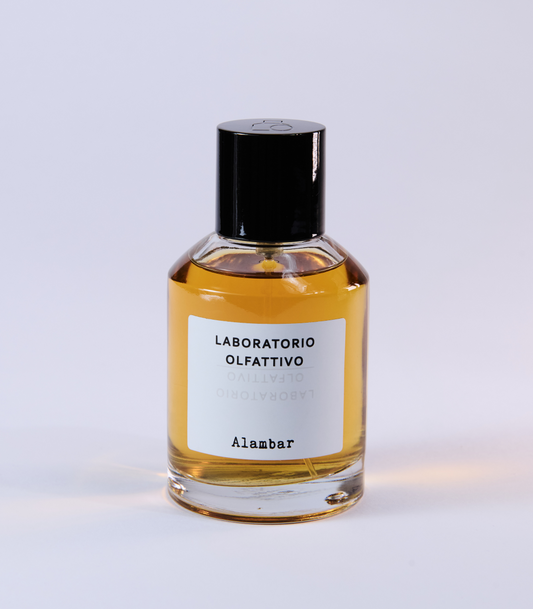 A clear glass bottle labeled Laboratorio Olfattivo Alambar, filled with amber-hued liquid, captures the refined fragrance of Alambar by Laboratorio Olfattivo, displayed against a simple light background.