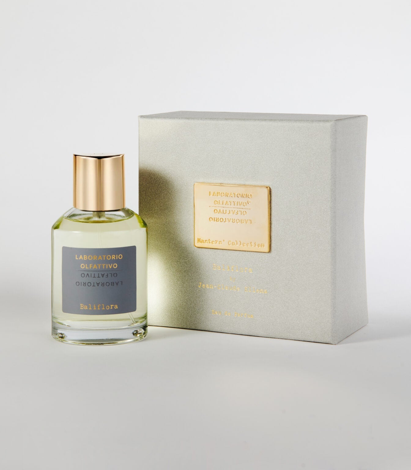 A clear glass perfume bottle with a gold cap labeled "Laboratorio Olfattivo Baliflora" stands beside a light gray box with a gold label, both on a white background—an elegant display inspired by White Lily and Ginger notes.