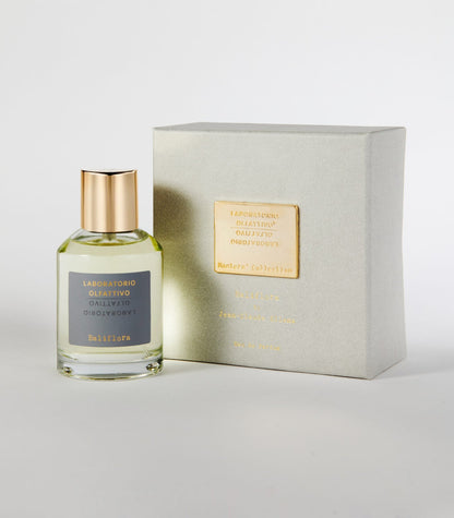 A clear glass perfume bottle with a gold cap labeled "Laboratorio Olfattivo Baliflora" stands beside a light gray box with a gold label, both on a white background—an elegant display inspired by White Lily and Ginger notes.