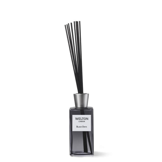 A rectangular glass bottle labeled Welton London holds the BLACK ONYX HOME FRAGRANCE DIFFUSER, featuring thin black reeds in a silver cap and releasing woody notes of vetiver, teak, and amber.