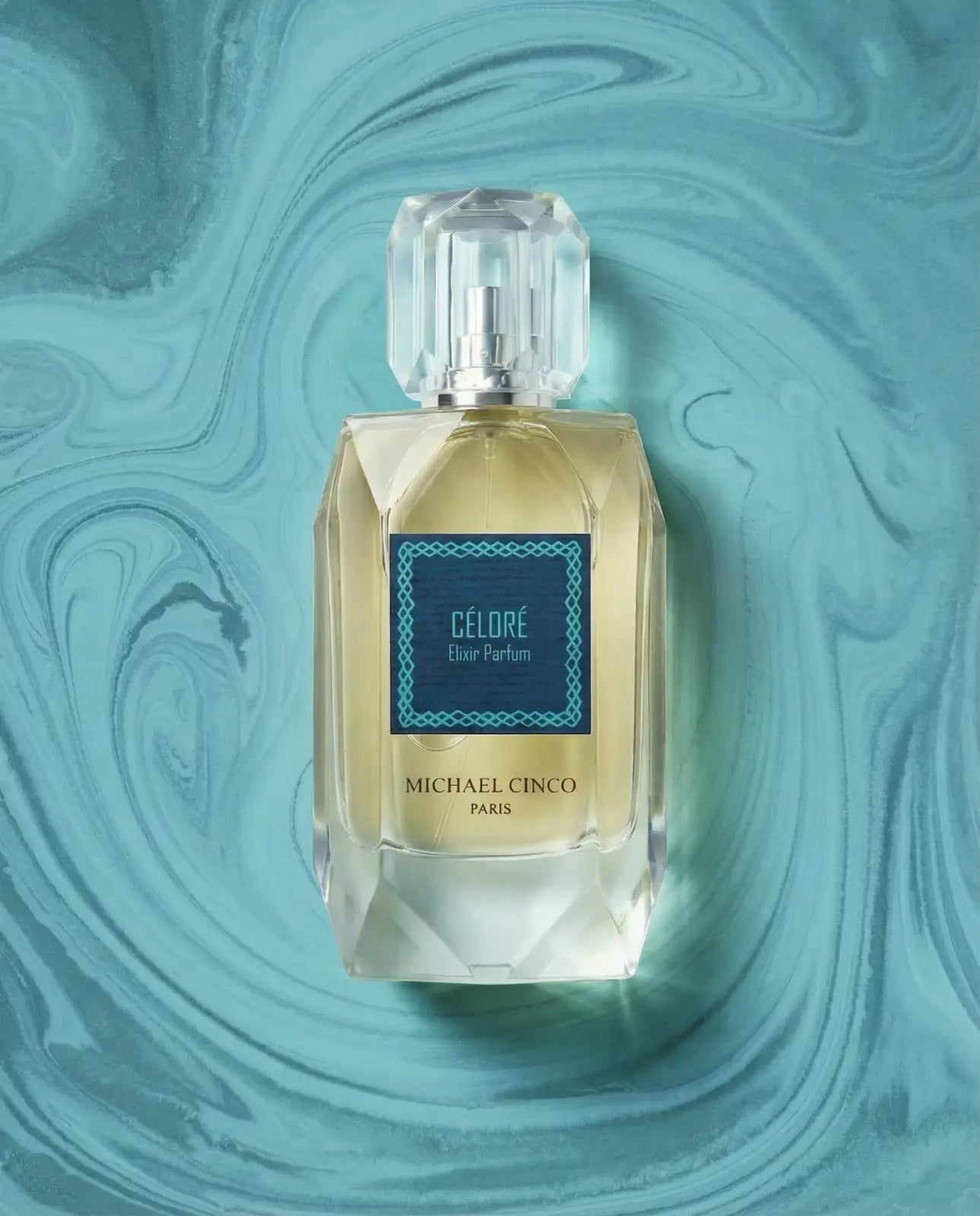 Michael Cinco Dior Parfum 'Céloré' perfume bottle, featuring a faceted clear glass design with a pale yellow liquid inside and a dark teal label, set against a matching teal marbled background.