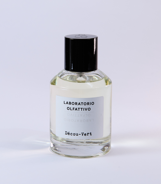 A clear glass bottle of Decou Vert Eau de Parfum by Laboratorio Olfattivo, with a black cap and minimalist label, stands against a plain background, evoking musky and woody notes inspired by a vibrant floral palette.