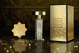A gold and black bottle of Lamar Caviar Eau de Parfum by Kajal Perfumes Paris rests beside its ornate box on a reflective surface, accented by scattered white caviar perfume pearls for a luxurious, elegant display.