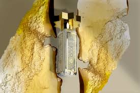 A decorative lantern with intricate patterns hangs between two large golden-yellow abstract shapes, evoking a dramatic scene inspired by the Lamar Caviar Eau de Parfum from Kajal Perfumes Paris.