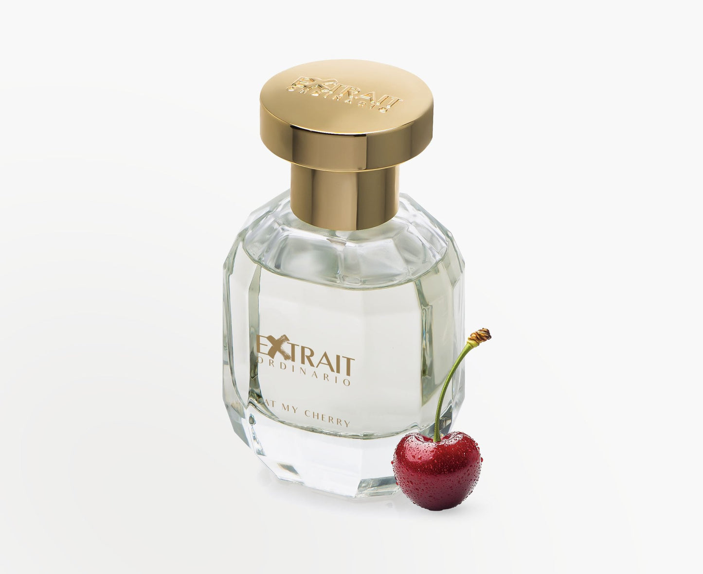 A clear glass bottle of Eat My Cherry - Extrait Ordinario by Extrait Ordinario, with a gold cap, stands beside a frosted cherry—a tempting invitation to experience this sensual fragrance against a crisp white background.