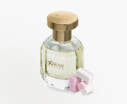 A clear glass Sweet Bubble - Extrait Ordinario perfume bottle with a gold cap from Extrait Ordinario stands beside three pink and white marshmallow candies, suggesting its bubble gum scent, all set against a white background.