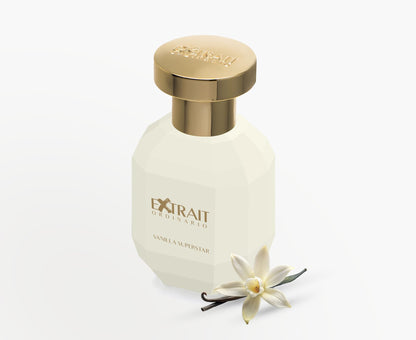 A white and gold Extrait Ordinario bottle labeled "Vanilla Superstar - Extrait Ordinario" stands upright beside a vanilla flower and bean, evoking the sweet, gourmand scent of this fragrance against a pristine white background.