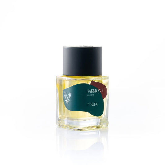 A clear glass bottle of Harmony Parfum by Fennec features a black cap, yellow liquid, and a dark green label with a white leaf, evoking the allure of North Africa and its graceful fennec fox. The bottle sits against a white background.