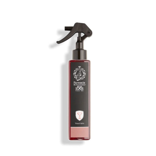 The Vinattieri Room Spray by Farmacia SS. Annunziata 1561 features a rectangular bottle with a black trigger nozzle, wine glass icon, and contains a reddish fruity wine-scented liquid for a refreshing air freshener experience.