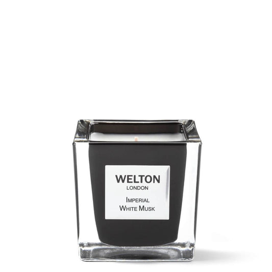 The Welton London IMPERIAL WHITE MUSK SCENTED CANDLE Classic features a square glass holder with a sleek black interior and centered wick, making it a sophisticated addition to any home. Label reads WELTON LONDON IMPERIAL WHITE MUSK. Background is plain white.