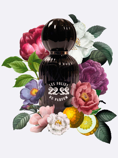A black bottle of 22.22 - Les Folies du Parfum by Les Folies du Parfum, handmade in Italy, sits among bright flowers and green leaves on a light background, highlighting its artistic and elegant design.