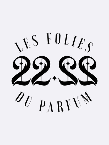 The image displays “22.22 - Les Folies du Parfum” in elegant serif and bold ornate fonts, centered on a light gray background—a nod to the artistic fragrances of Les Folies du Parfum.