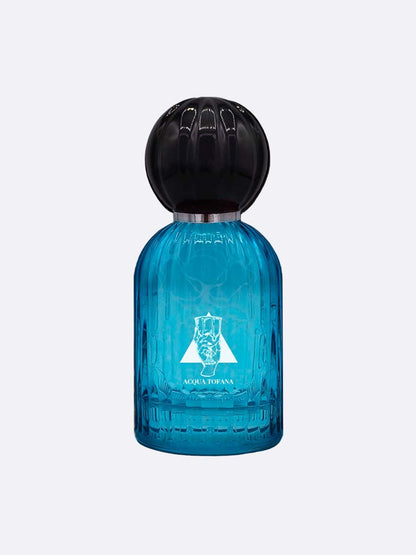 A blue glass perfume bottle with a large round black cap. The front shows a white emblem and “Acqua Tofana - Les Folies du Parfum” by Les Folies du Parfum, evoking a seductive scent. The background is plain and light-colored.