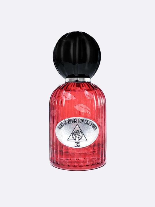 A red ribbed glass perfume bottle with a black cap labeled Les Folies du Parfum BX, featuring a triangular logo with a face, evokes a sensual scent inspired by the bold Countess of Castiglione.