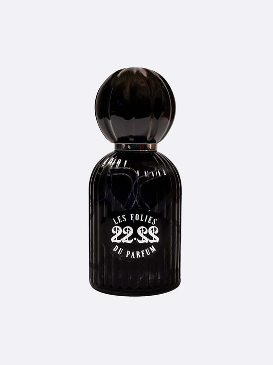 A black, ribbed glass bottle with a rounded cap displays the label "22.22 - Les Folies du Parfum" by Les Folies du Parfum, handmade in Italy, above a white design of three intertwined snakes on a plain light gray background.
