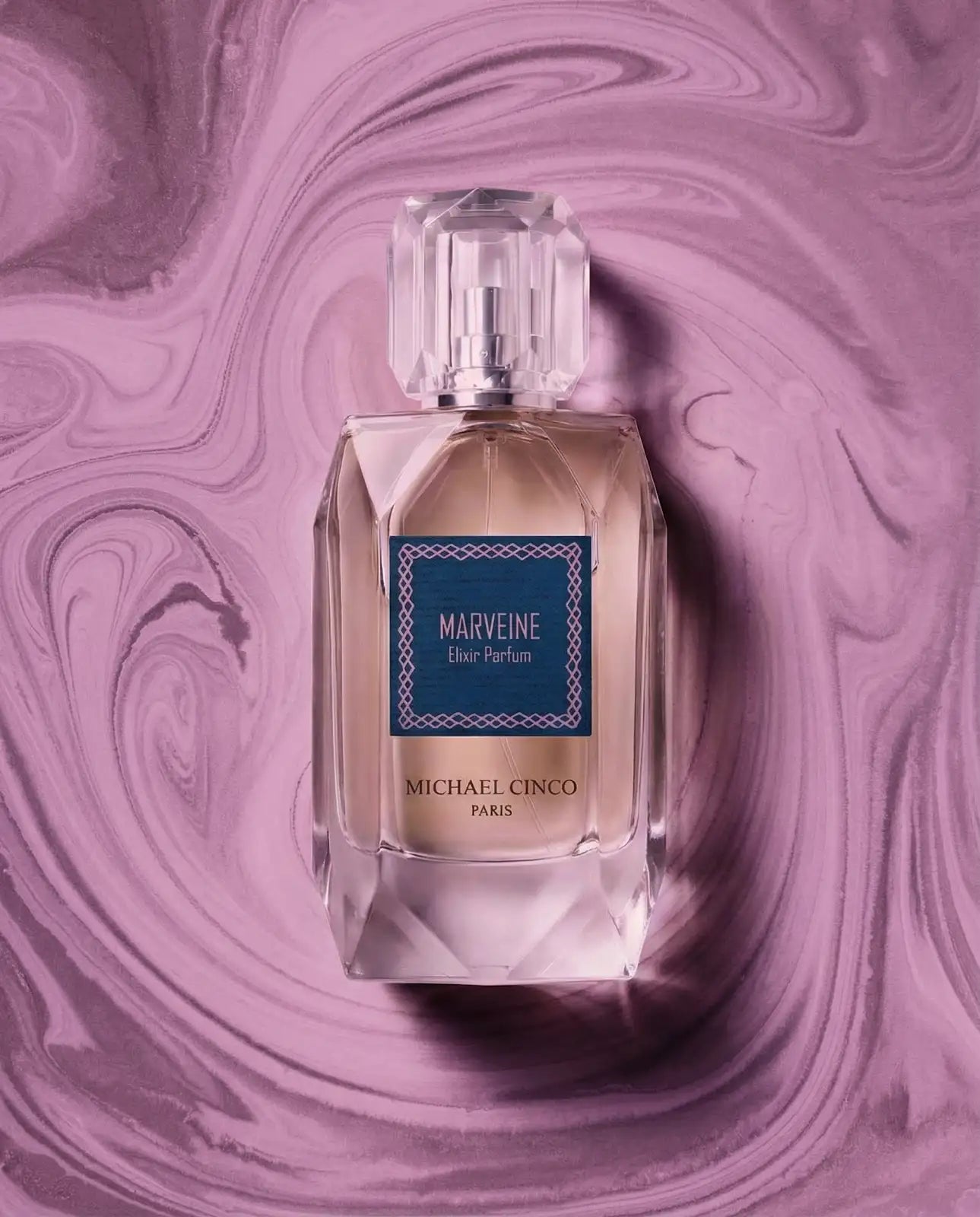 Michael Cinco Marveine Eau de Parfum bottle centered on a swirling purple and pink marbled background. The clear glass bottle contains a pale amber liquid and features a blue label with white text.