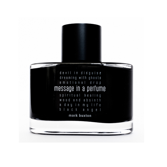 A black bottle of MESSAGE IN A PERFUME Eau de Parfum by Mark Buxton, featuring white text with phrases like devil in disguise, spiritual healing, and a day in my life—an island-inspired fragrance called Paradise.