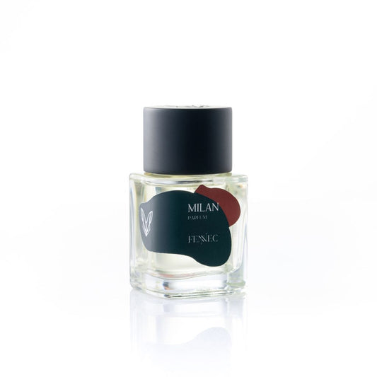 A clear glass Milan Parfum bottle by Fennec, featuring a black cap and an abstract green and red label, inspired by the elegance of the North African desert fox, set against a white background.