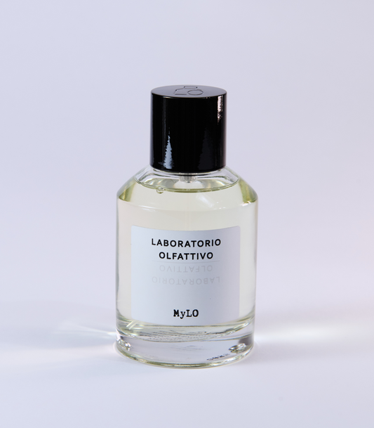 A clear glass bottle of MyLO - Laboratorio Olfattivo perfume by Laboratorio Olfattivo, featuring a black cap and white label, stands on a light surface—an elegant showcase of floral fragrance.