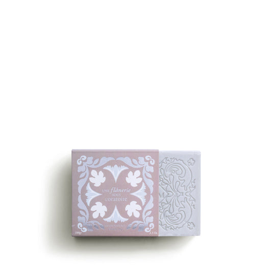 The ROSE ET MARIUS SCENTED SOAP by Rose Et Marius, a rectangular natural bar with exfoliating grape seeds, is partially slid from a pink and white floral box; both display intricate patterns against a plain white background.