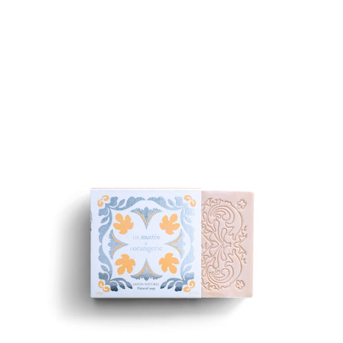 A rectangular ROSE ET MARIUS SCENTED SOAP by Rose Et Marius, featuring an ornate design, sits beside its box adorned with a blue, white, and yellow floral pattern labeled “L’Orangerie.” Both made in France and shown on a white background.