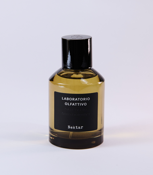 A bottle of Nektar Eau de Parfum by Laboratorio Olfattivo, featuring a black label and cap and inspired by the sweetness of Sidr Honey, displayed on a plain, light-colored background.