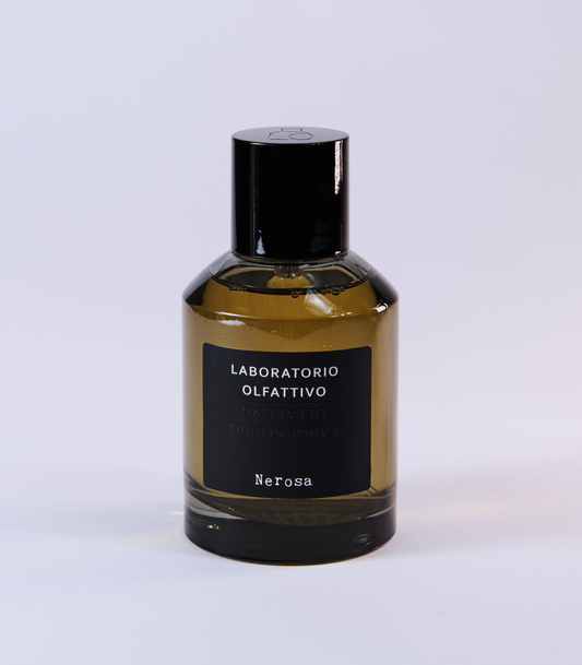 A brown glass bottle of Nerosa Eau de Parfum by Laboratorio Olfattivo, with a black cap and label, made from natural raw materials, rests on a plain light background.