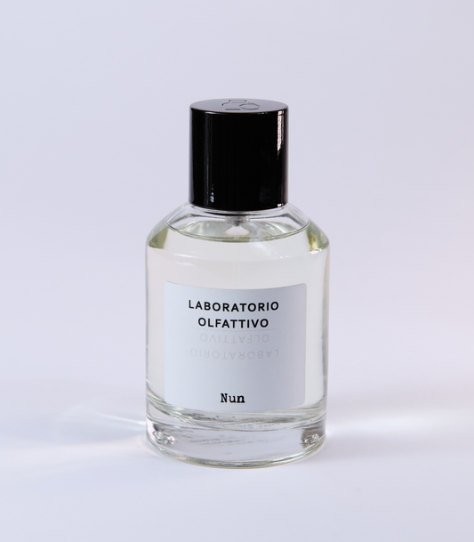 A clear glass bottle of NUN Eau de Parfum by Laboratorio Olfattivo with a black cap, displayed on a white background, highlights the allure of lotus jasmine notes and exquisite amber musk.