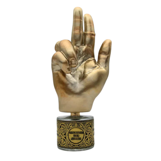 A gold-toned hand sculpture with a three-finger gesture stands on an ornate base engraved "Geser Die Aries," evoking vanilla and amber, showcased against white. Product: SACRISTIE DES ARBRES "Tree Vestry" Eau de Parfum by Filippo Sorcinelli.