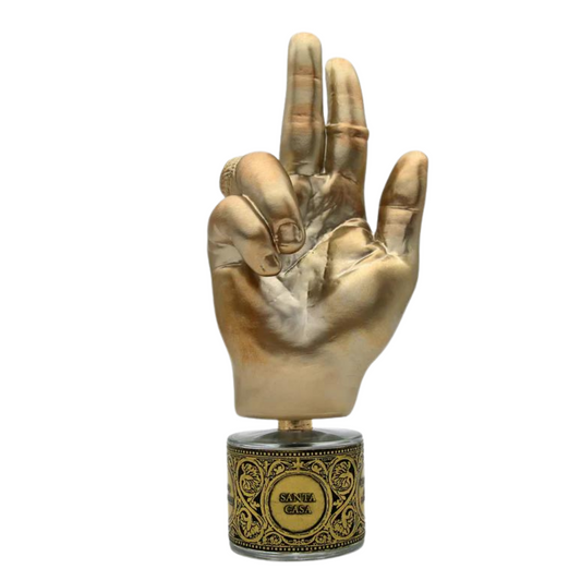 A golden hand sculpture with three fingers raised, mounted on an ornate base inscribed "SANTA CASA," captures the essence of Filippo Sorcinelli's SANTA CASA "Holy House" Eau de Parfum, evoking a serene Marian sanctuary aura.