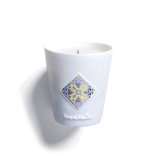 The ROSE'S SUN WATER "SCENTED CANDLE L'EAU ENSOLEILLE DE ROSE” by Rose Et Marius comes in a refillable Limoges porcelain holder with a raised square tile design in yellow, gray, and lavender, and “Rose et Marius” embossed below the decorative tile.