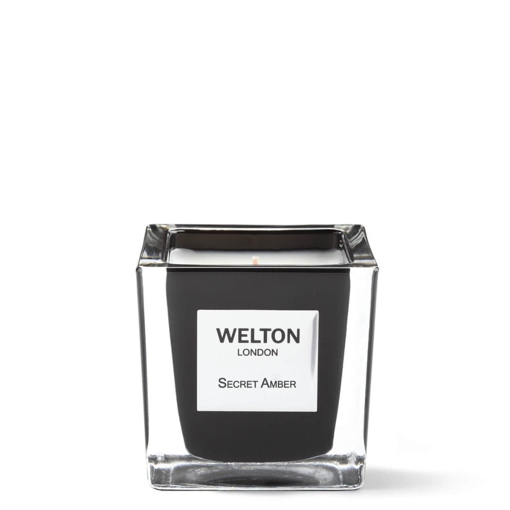 The SECRET AMBER SCENTED CANDLE Classic by Welton London features a square glass holder with black branding and a white candle, infused with subtle white jasmine notes, displayed elegantly against a white background.