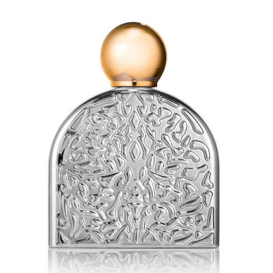 SENSUAL Eau de Parfum by M.Micallef features a textured, abstract silver bottle with a smooth gold cap, elegantly displayed on a reflective surface—an exquisite vessel for this oriental floral fragrance against a white background.