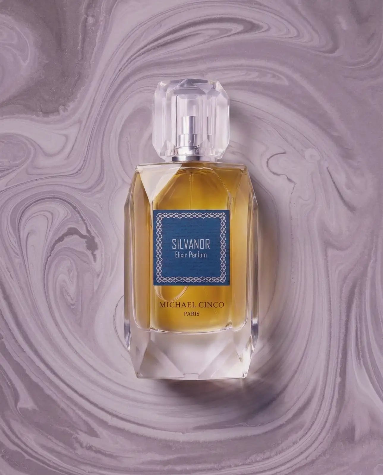A bottle of Michael Cinco Silvandor Eau Parfum with golden-yellow liquid and a blue label, centered on a purple marbled background.