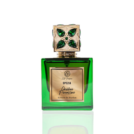 A green glass bottle of Spezia Eau de Parfum by Christian Provenzano, with a jeweled gold cap accented in green, evokes luxury and the essence of a Tuscan vineyard, set against a white background.